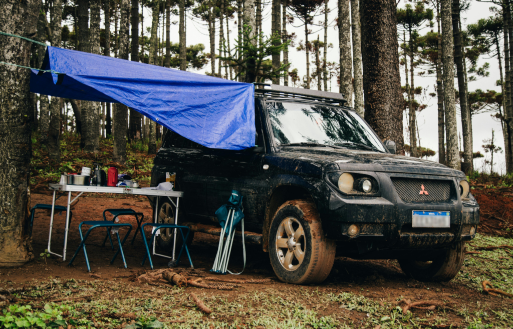 Off-Road Car Standing by Picnic Place in Forest with blue tarp 