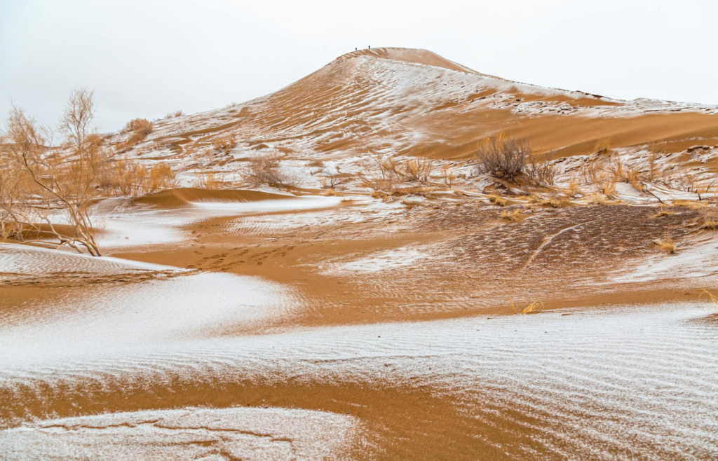 A desert landscape with sand dunes partially covered in snow