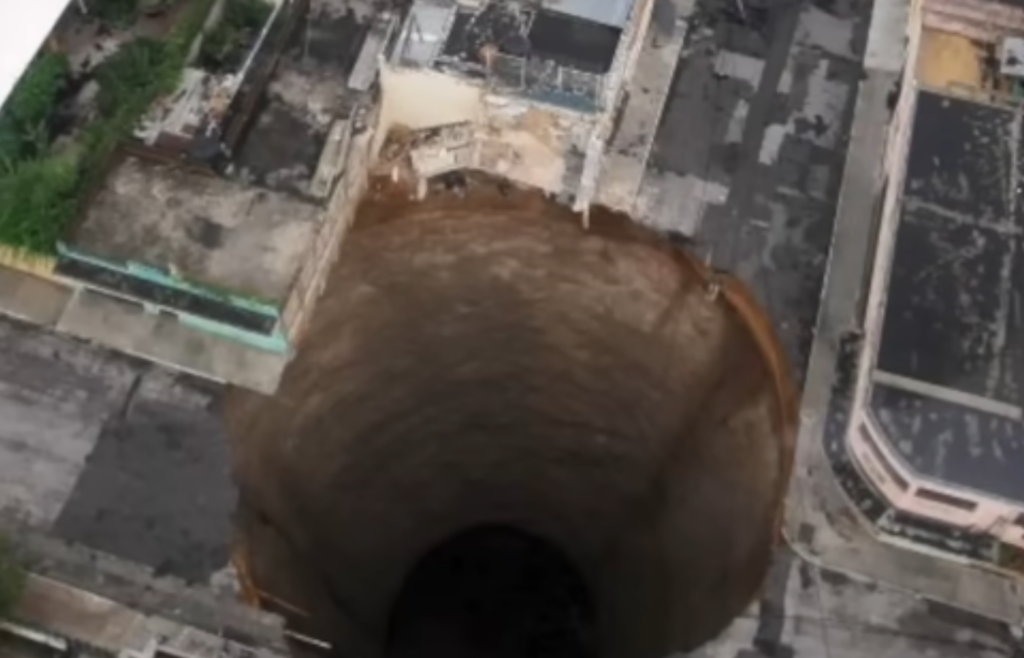 Massive sinkhole in urban area with damage.