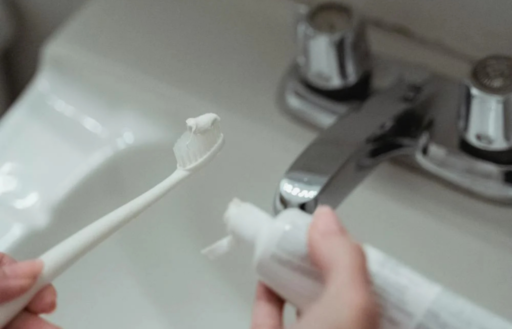A person turning off a faucet while brushing their teeth