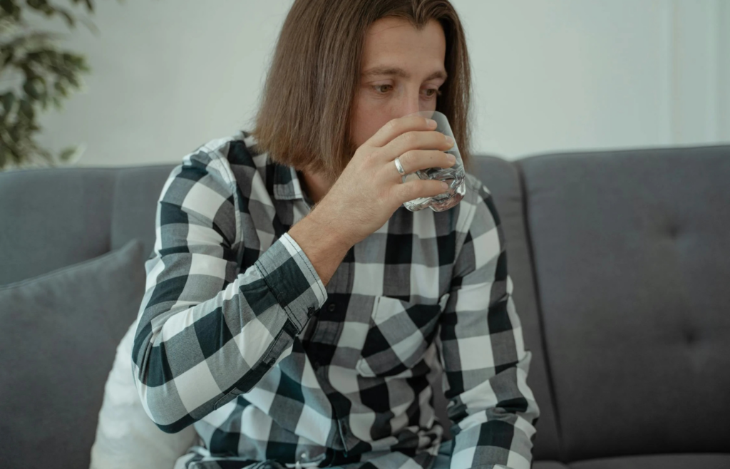 Person smelling a glass of water with a displeased expression