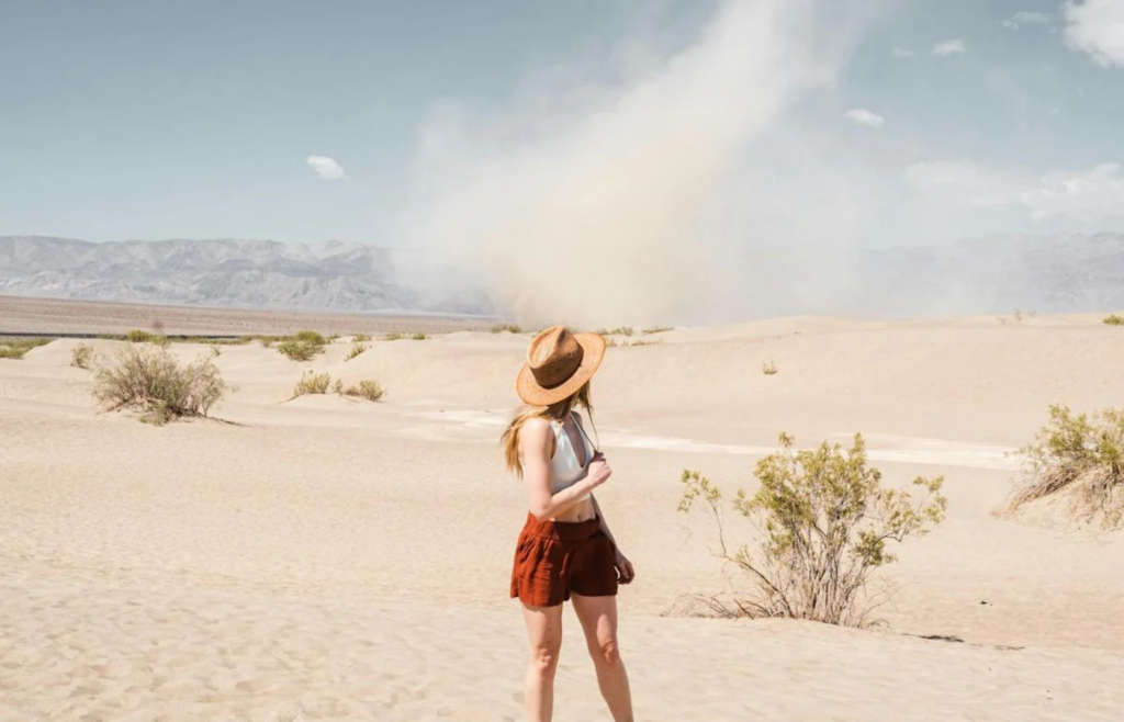 Woman in a desert, watching a dust devil twist across the sands