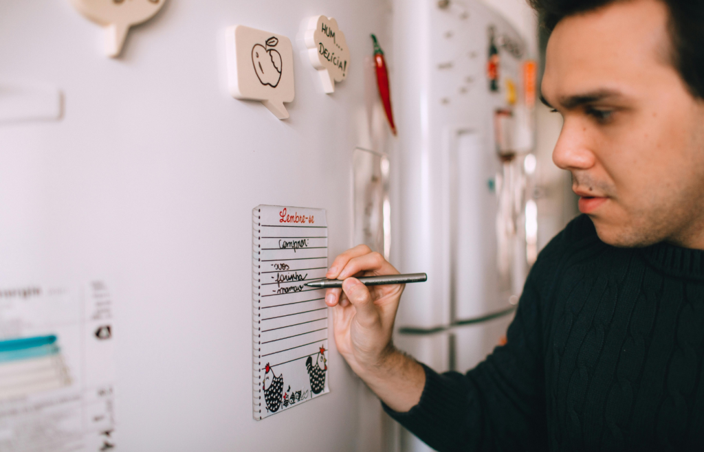 Young man writing reminder on fridge note